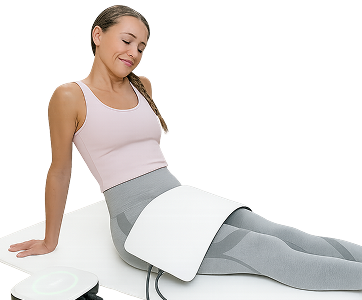 Frau sitzt entspannt auf Matte, eine große weiße Therapieapplikatorplatte liegt über ihrem Becken, verbunden mit einem Sanza-Gerät